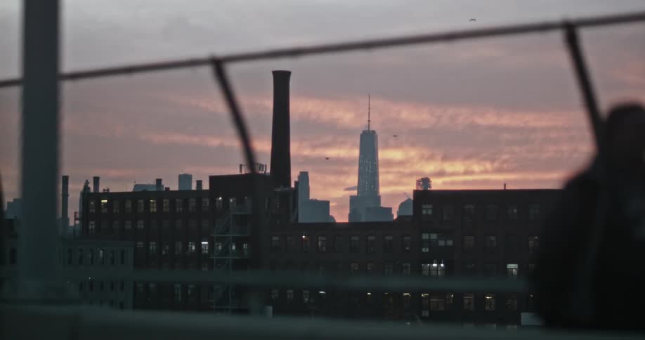 A person watches a pink sunset behind a large building