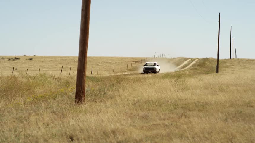Pickup truck drives down a dirt road next to wheat fields