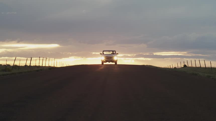 A car approaches appearing over the horizon at sunset