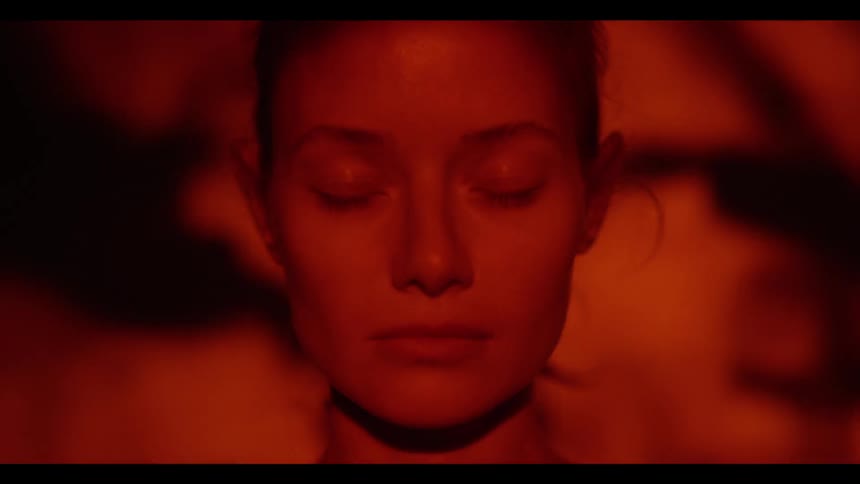 Close up of a woman opening and closing her eyes as orange colored images are projected over her