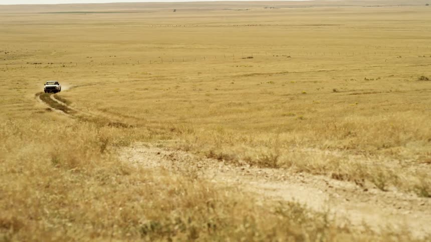 A truck driving down a dirt path in a field