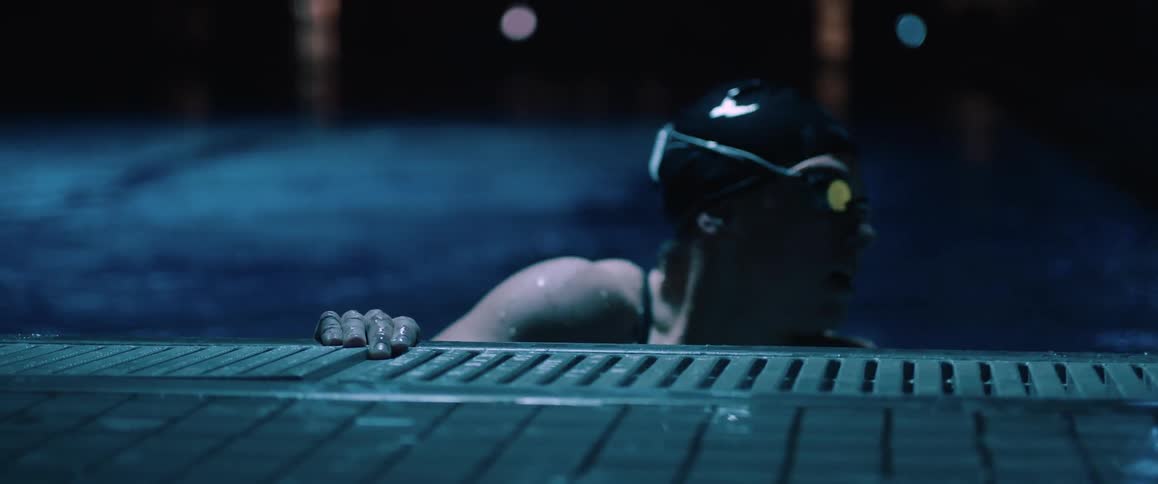 A woman with her arms resting on the edge of a pool before she turns and swims away