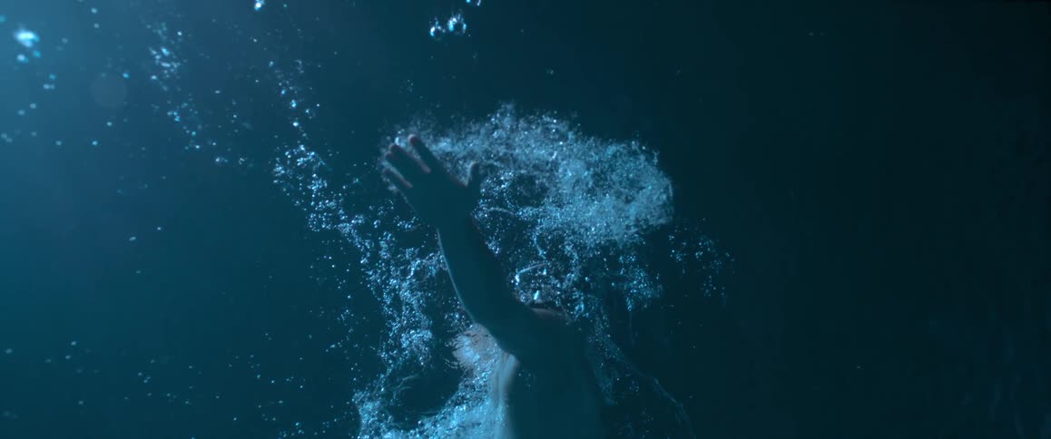 Slow motion, underwater shot of a man swimming and bubbles trailing him in a dark pool area
