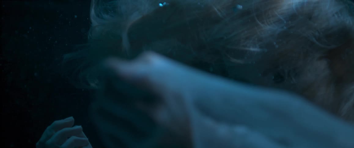 A woman in a white dress moves in slow-motion while under water