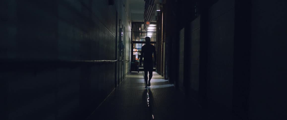 Man walking down a dark hall with a flag overhead