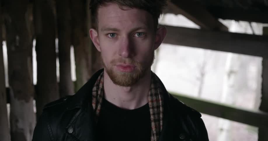 A young man stands inside a barn while staring into the camera