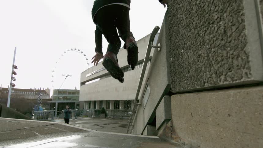 A man riding rollerblades jumps up onto the metal railing of an outdoors flight of stairs