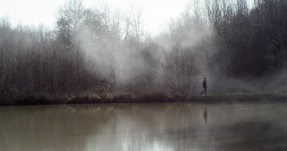 A man walking alongside a foggy lake