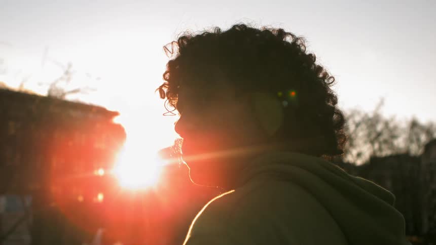 Young man walks down a city street as the sun shines