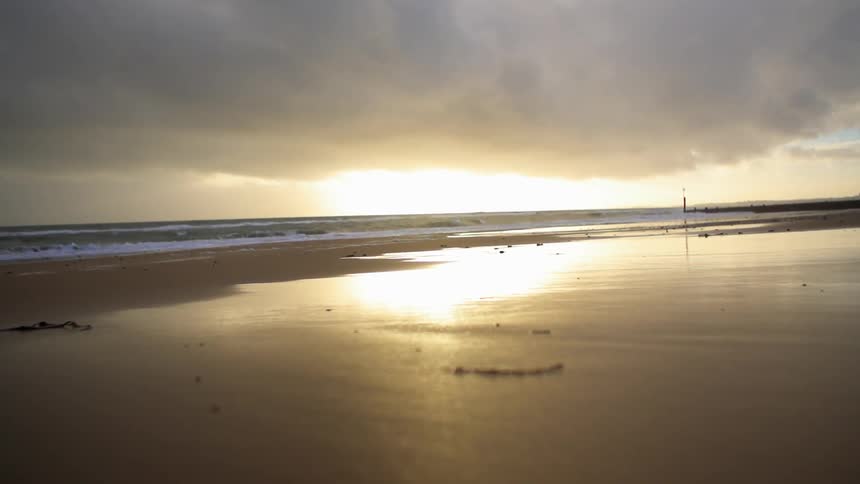 View of wet sand as waves crash on a shore at sunrise