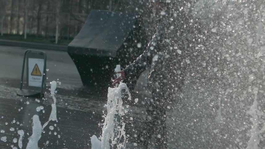 Water shooting up and falling back down as someone roller blades through it in an urban area