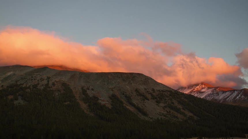Time lapse of clouds moving over mountains peaks that are brilliantly colored by the sun