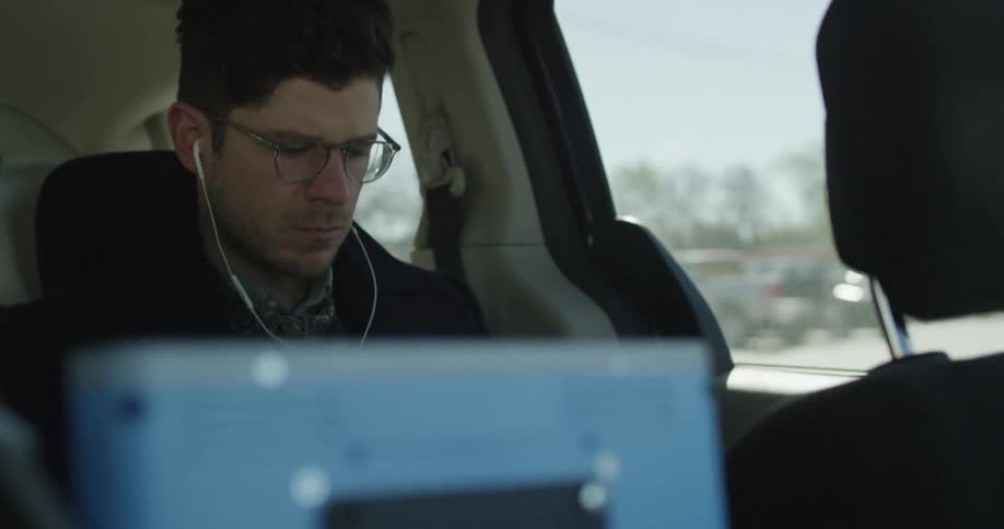 A man in glasses wearing headphones rides in a vehicle