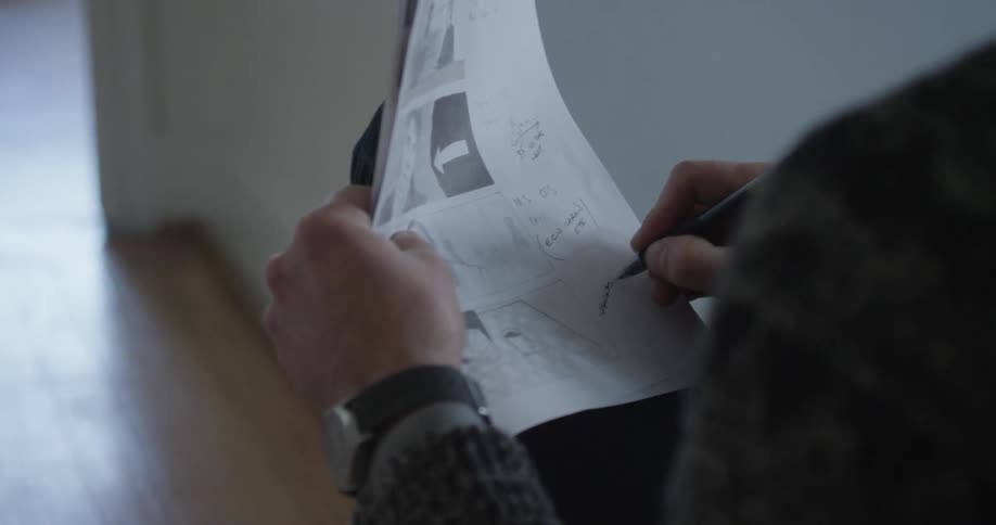 A man in gray sweater makes notes on a set of drawings