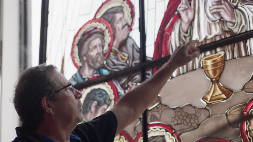 Older man points at stain glass of religious image