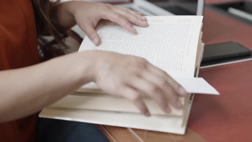 Student looking through book by laptop