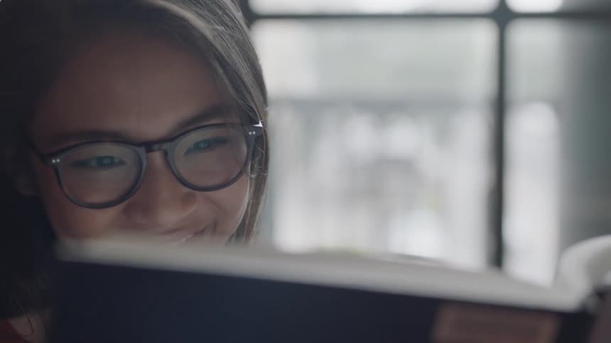 Asian woman smiling as she looks at a book