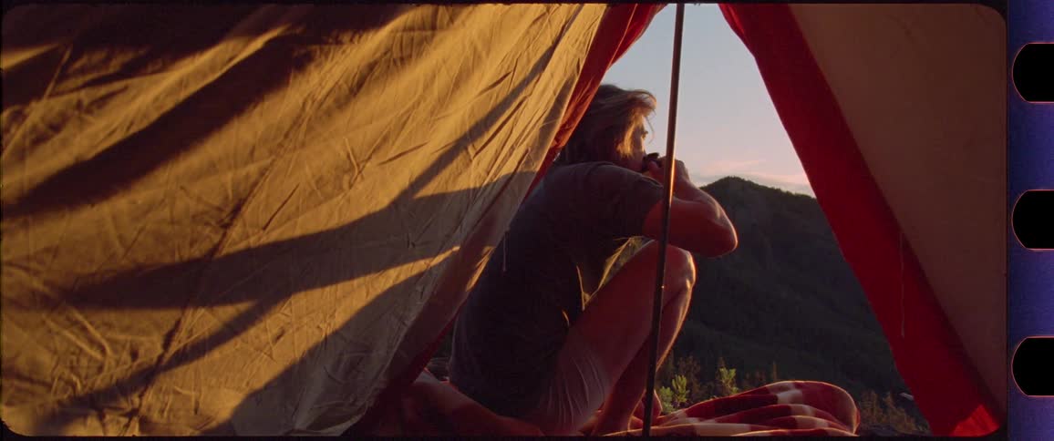 Man drinking coffee in front of his tent with mountain scenery in the background