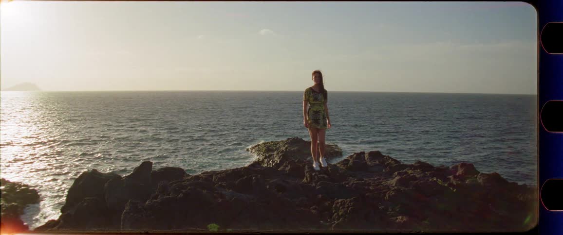Woman in a dress walking on rocks next to the ocean while enjoying the sunset