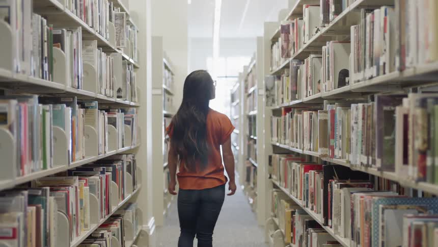 Student looking for book in a library aisle