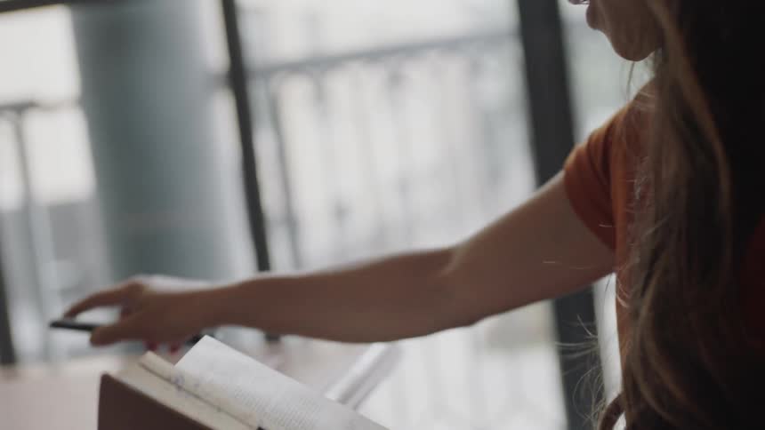 Young woman with glasses looking at phone and then book