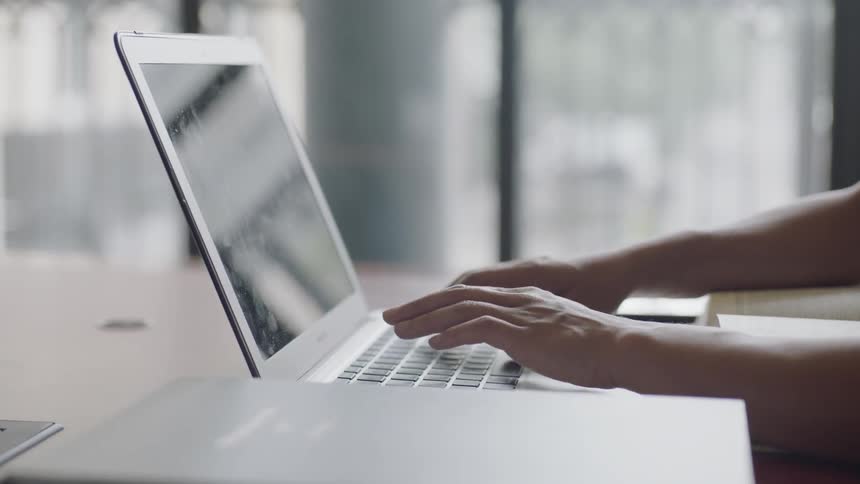 Typing on laptop in front of large window