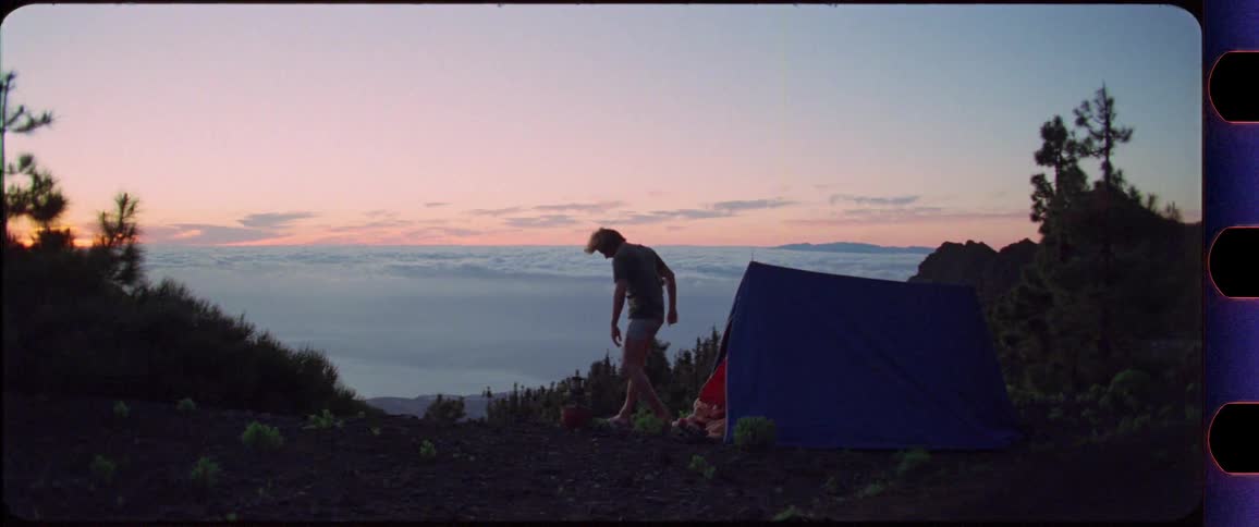Man stretching in front of his tent on top of a mountain at sunrise overlooking the clouds