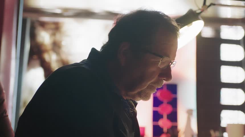 Man wearing glasses looking down with lamp behind him