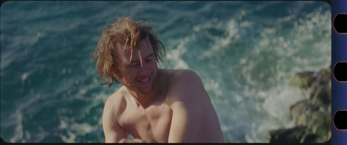 Topless guy with wet hair enjoys the sun by the ocean