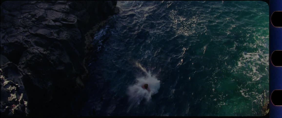 Man jumps off a cliff into the ocean while the sun is setting
