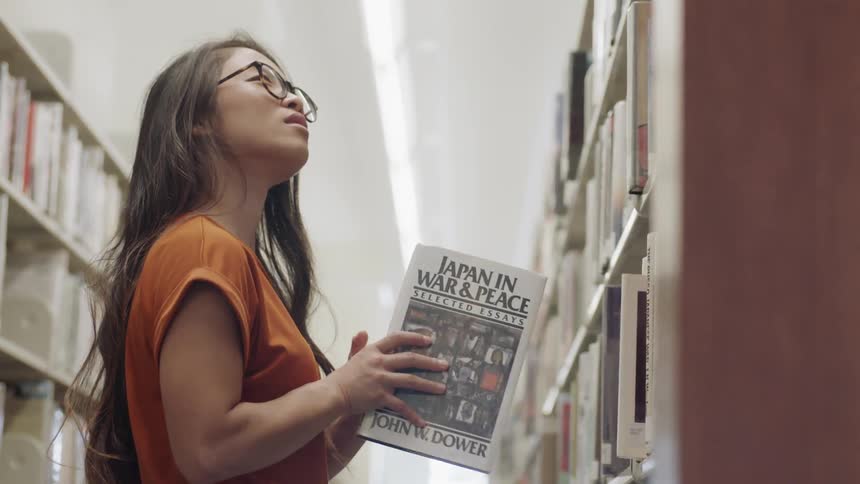 Asian woman putting book back on shelf in library