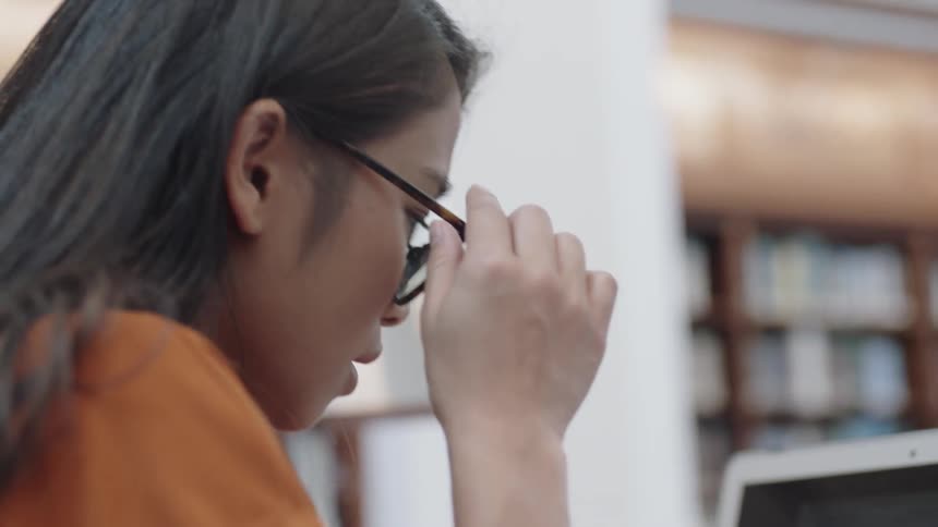 Student touching glasses and looking at computer