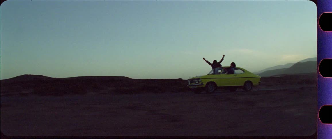 yellow car racing through the desert with people climbing out the window