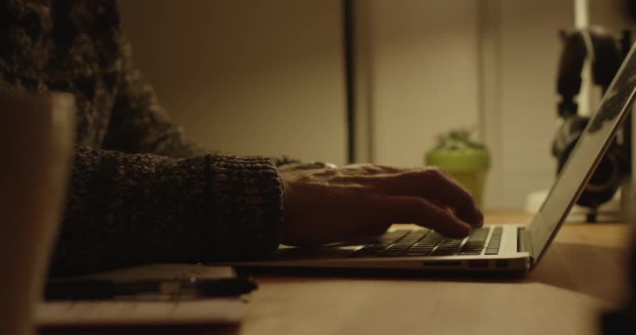 A man types on a laptop keyboard and then crosses an item off a list
