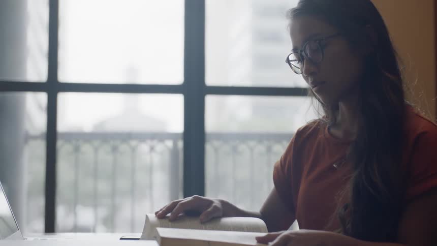 Young woamn looking out window before tryping on laptop