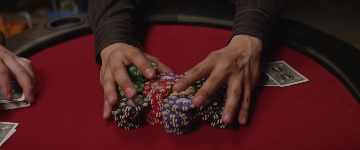 Man smoking and pushing a pile of poker chips on a card table