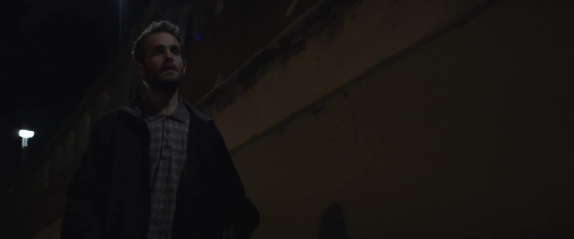 A man walking on an urban street at night lights a cigarette