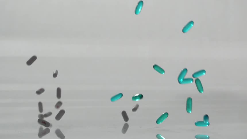 Various pill capsules fall onto a grey, reflective surface