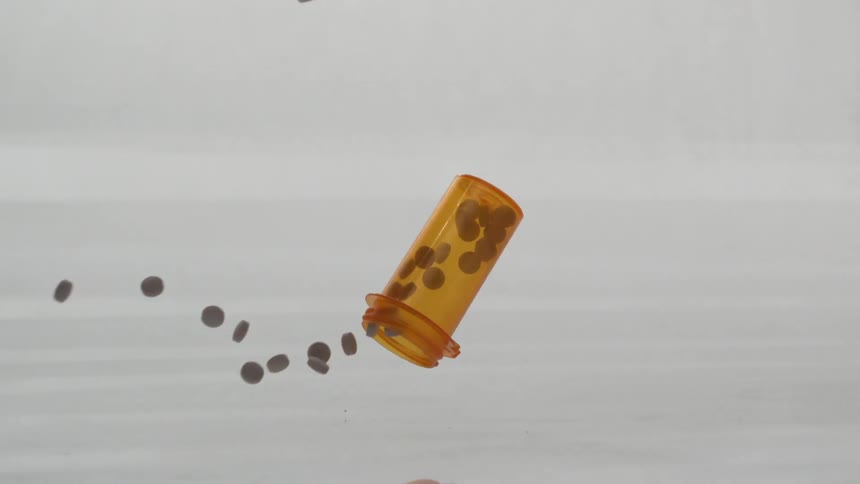 A prescription bottle of pills hits the surface and the pills fall out