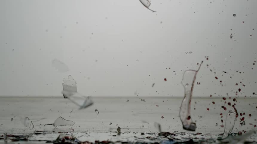A wine glass hits the surface and shatters spilling red wine
