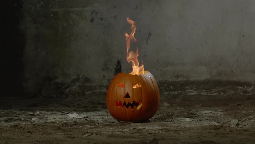 A jack-o-lantern sits on the ground with flames coming out its top