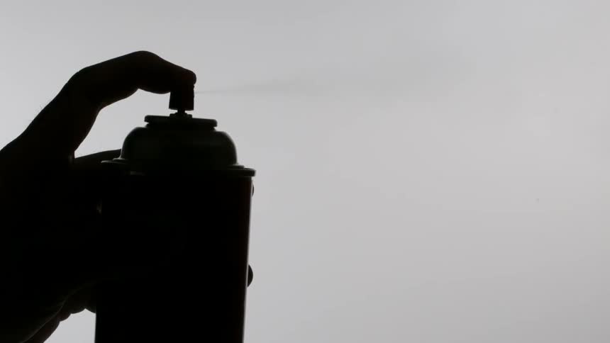 A finger presses the head on a spray can