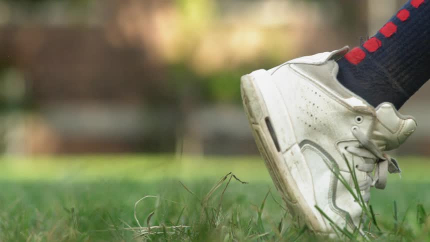 Person wearing white sneakers running on grass in slow motion
