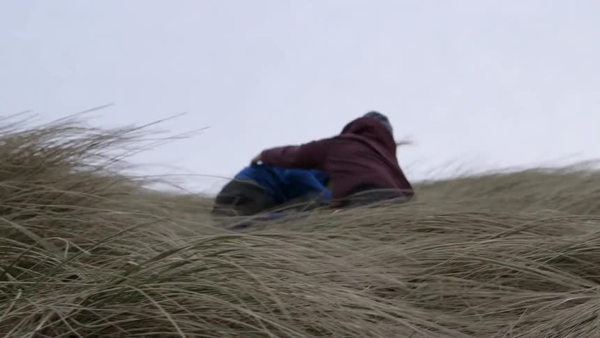 A man and woman roll down a hill on a windy day