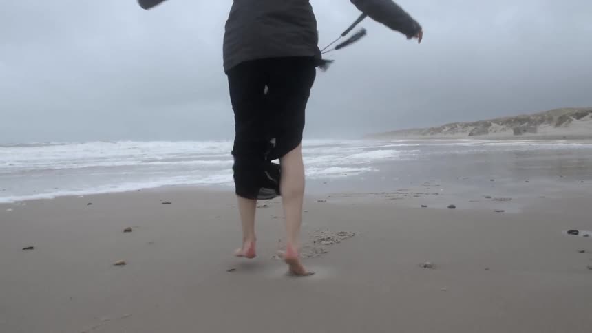 A woman in a coat and flowing skirt twirls on the beach
