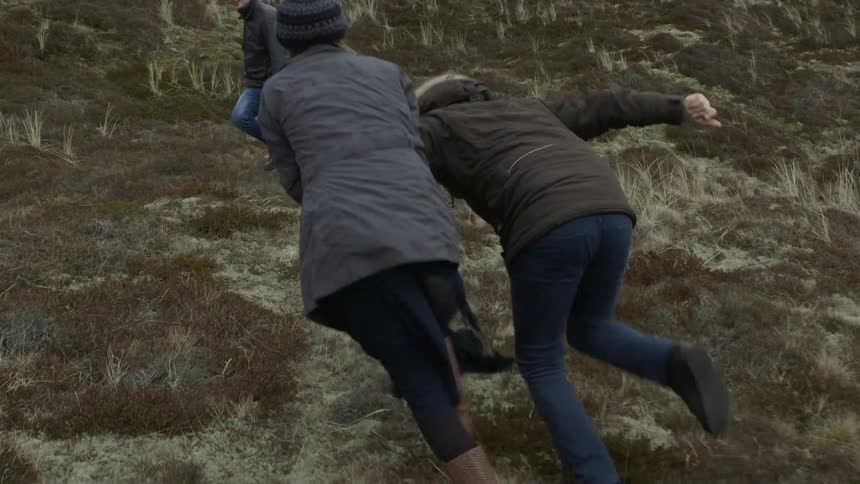 Three people playing and running uphill on a cloudy day