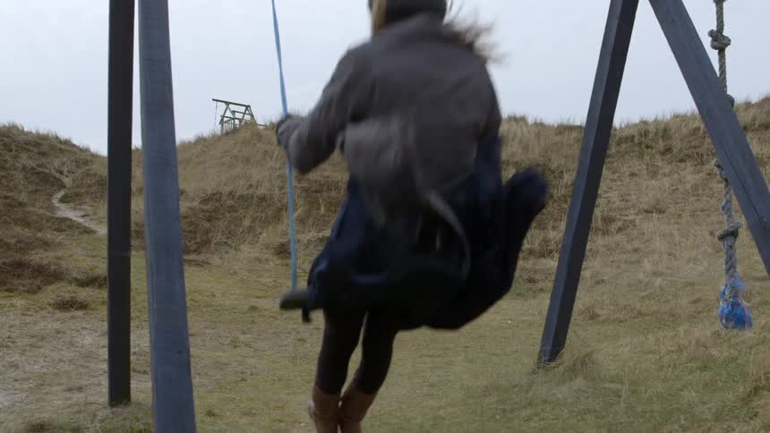 A woman wearing a heavy coat and knit cap swings on a swing set