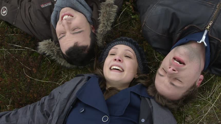 Two men and a woman lying on the ground singing and laughing