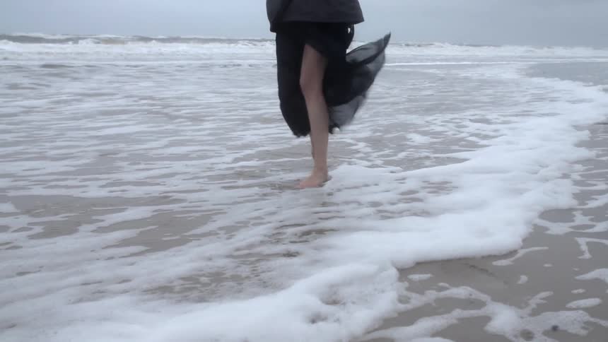 A woman spins and dances on a windy beach