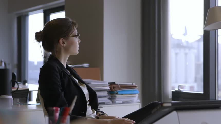 Woman looking at a desk and pushing it away before looking the window